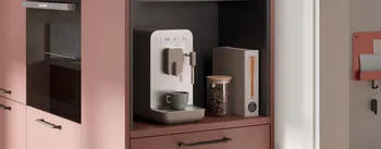 Detailansicht einer modernen Küche mit eingebauter Kaffeemaschine, Glasbehälter mit Kaffeebohnen und Deko. Warmes Farbkonzept in Rosé-Tönen mit eleganten Griffen und harmonischem Küchendesign.